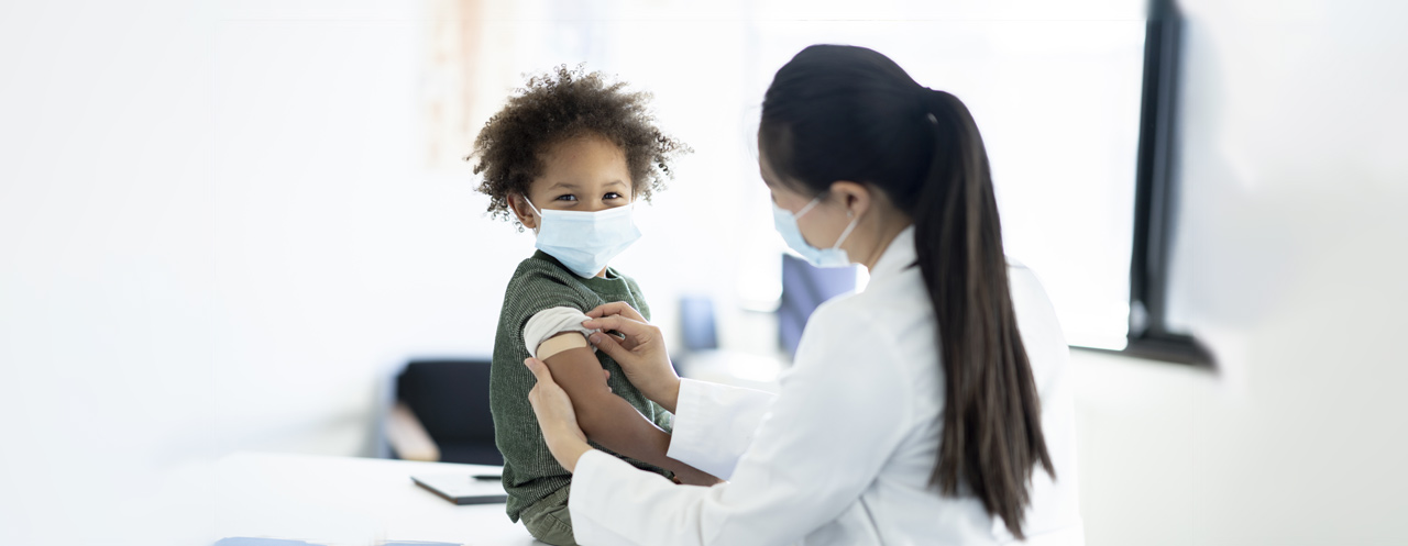A healthcare provider applying a bandaid to a young patient's arm.